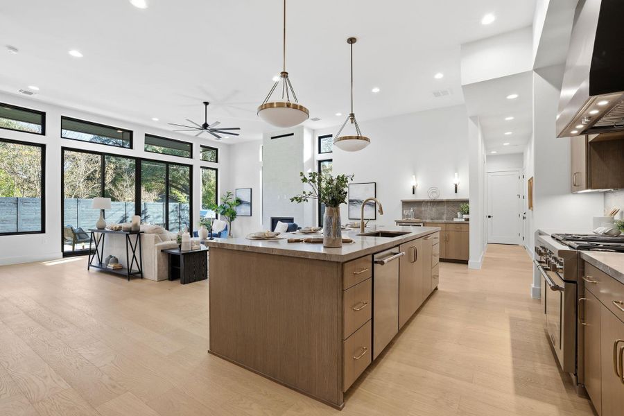 Kitchen with ceiling fan, light wood finished floors, an island with sink, light stone countertops, and recessed lighting