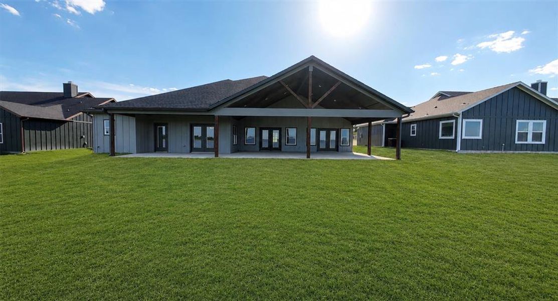 Expansive green lawn with a covered patio featuring exposed wood beams and support pillars Expansive green lawn with a covered patio featuring exposed wood beams and support pillars