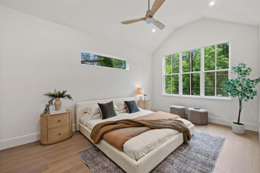 Vast windows flood this spacious bedroom with natural light, complementing the vaulted ceiling and warm wood flooring.