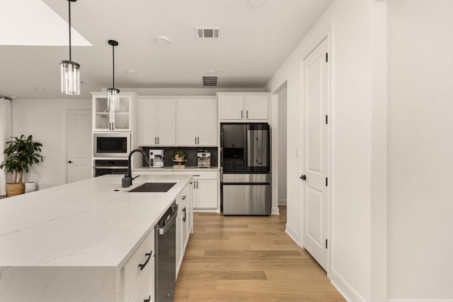 Contemporary kitchen featuring an oversized island with an integrated sink and dishwasher, white cabinetry, stainless steel appliances, and wood-finish flooring