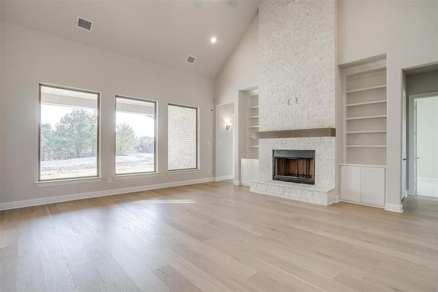 Unfurnished living room with built in shelves, ceiling fan, high vaulted ceiling, light hardwood / wood-style floors, and a fireplace