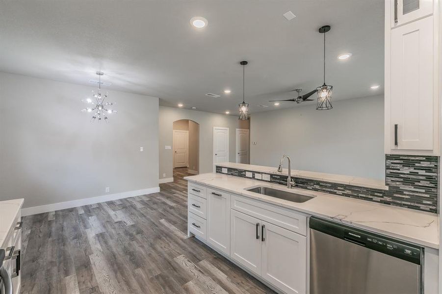 Kitchen featuring hanging light fixtures, hardwood / wood-style flooring, white cabinets, sink, and dishwasher