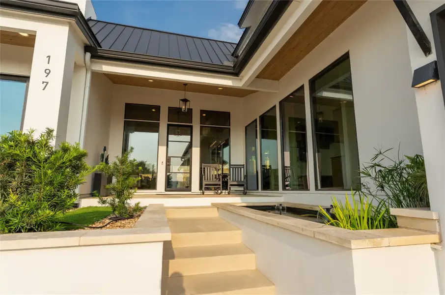 Contemporary exterior featuring a white stucco finish, a dark metal roof, large fixed-pane windows, a recessed entry with wood-finish soffit, and a built-in water feature Contemporary exterior featuring a white stucco finish, a dark metal roof, large fixed-pane windows, a recessed entry with wood-finish soffit, and a built-in water feature