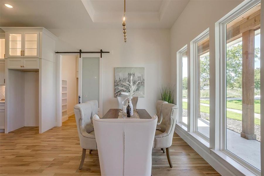 Dining area with light wood-type flooring, a barn door, and a tray ceiling