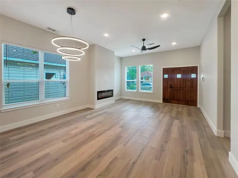 Unfurnished living room with visible vents, light wood-style floors, baseboards, a glass covered fireplace, and ceiling fan with notable chandelier Unfurnished living room with visible vents, light wood-style floors, baseboards, a glass covered fireplace, and ceiling fan with notable chandelier