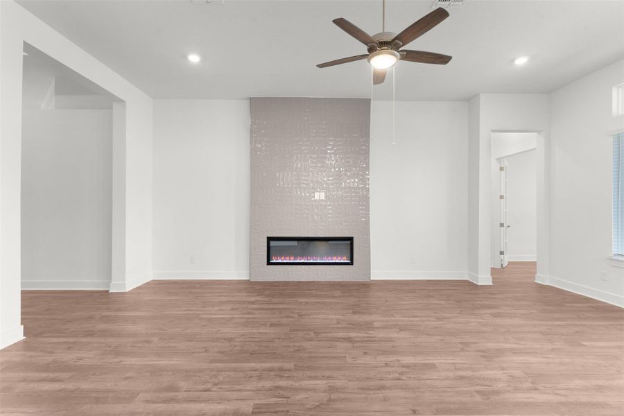 Unfurnished living room featuring light wood-style flooring, a large fireplace, ceiling fan, and recessed lighting