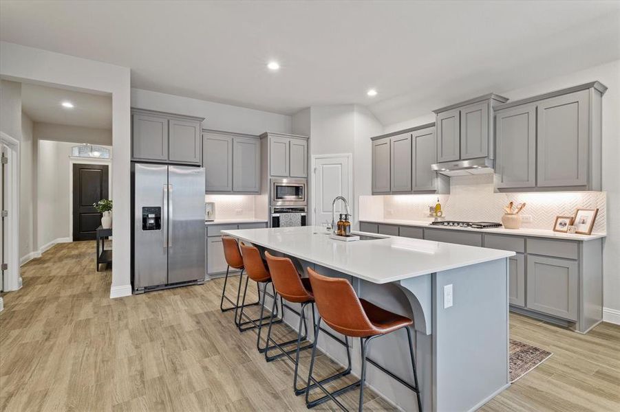 Kitchen featuring decorative backsplash, sink, a center island with sink, appliances with stainless steel finishes, and light hardwood / wood-style flooring