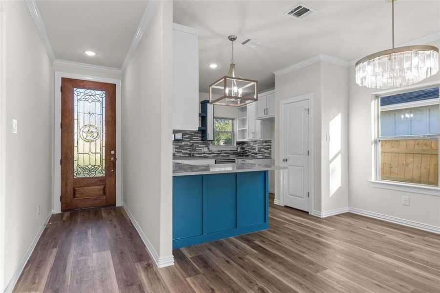 Kitchen with white cabinets, ornamental molding, decorative backsplash, a chandelier, and dark wood-type flooring