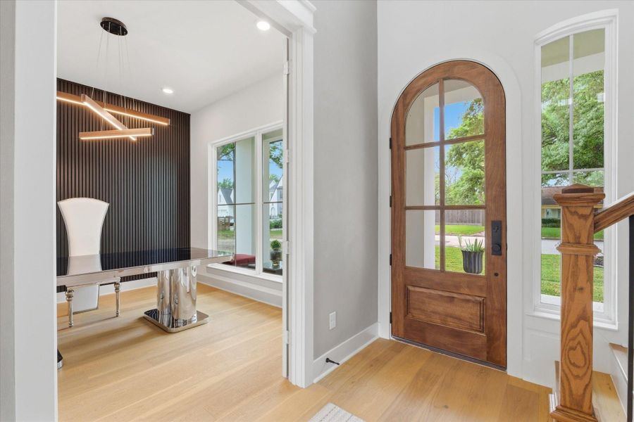 Office located just off the entry, featuring a modern light fixture, ample windows, and a fluted wood accent wall.