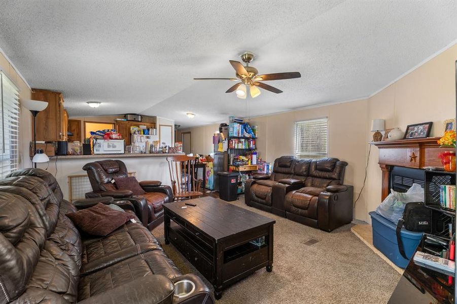 Carpeted living room featuring a fireplace, ornamental molding, ceiling fan, vaulted ceiling, and a textured ceiling Carpeted living room featuring a fireplace, ornamental molding, ceiling fan, vaulted ceiling, and a textured ceiling