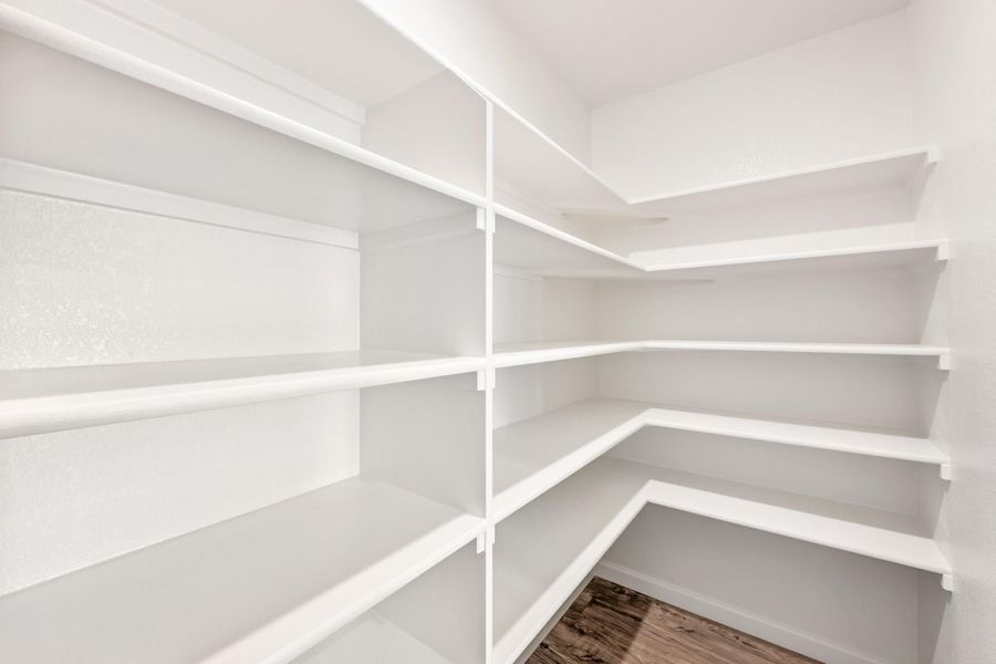 Walk-in pantry with white built-in shelving on two walls and wood-look flooring