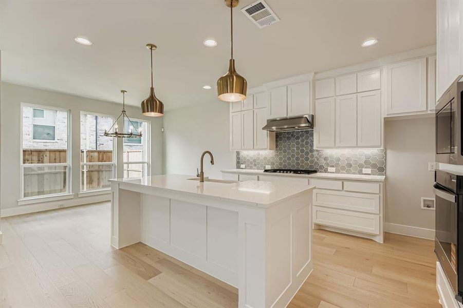 Kitchen featuring under cabinet range hood, light countertops, tasteful backsplash, light wood finished floors, and recessed lighting