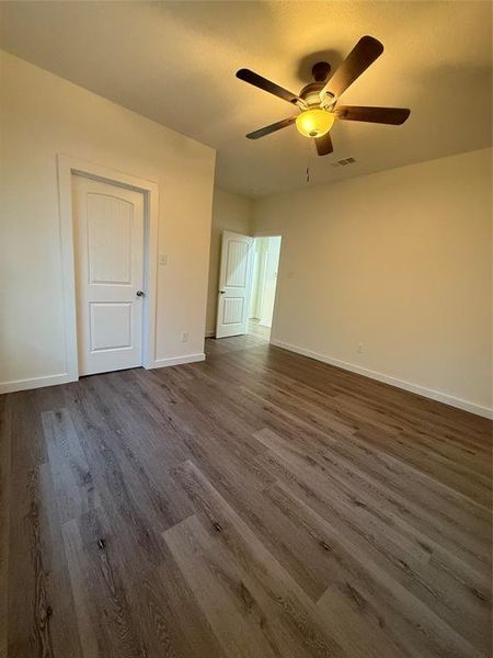 Unfurnished room featuring a ceiling fan, dark wood finished floors, visible vents, and baseboards