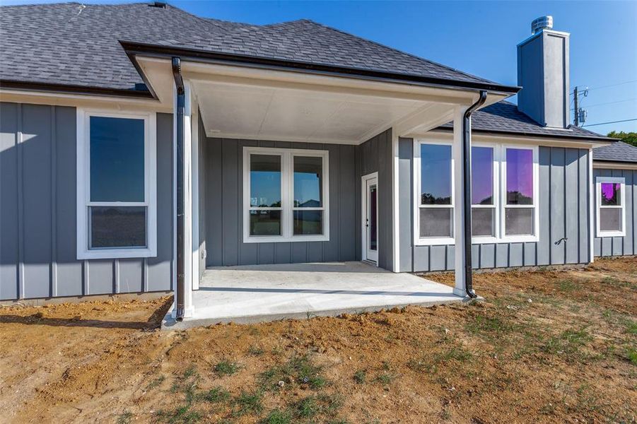 Rear view of property with board and batten siding, roof with shingles, a patio, and a chimney Rear view of property with board and batten siding, roof with shingles, a patio, and a chimney