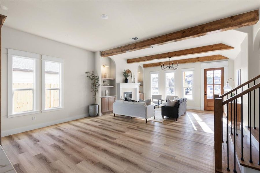 Living room with a chandelier, beam ceiling, built in shelves, and light hardwood / wood-style flooring