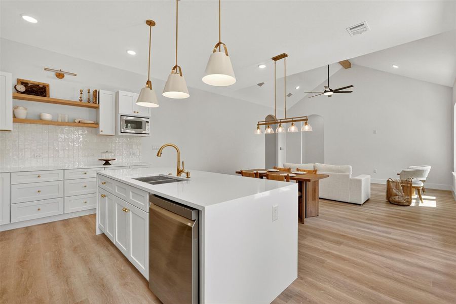 Kitchen featuring white cabinetry, hanging light fixtures, backsplash, a ceiling fan, and light wood-style flooring