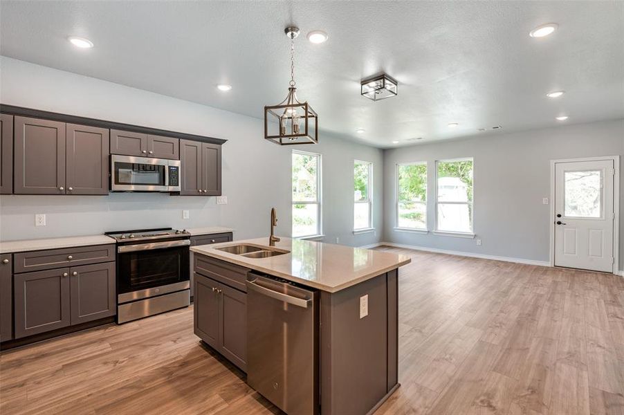 Kitchen with appliances with stainless steel finishes, a center island with sink, sink, light hardwood / wood-style floors, and decorative light fixtures