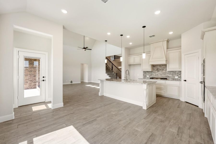 Open-concept kitchen with white cabinets, granite island, tile backsplash, and wood-look floors flowing into living area Open-concept kitchen with white cabinets, granite island, tile backsplash, and wood-look floors flowing into living area
