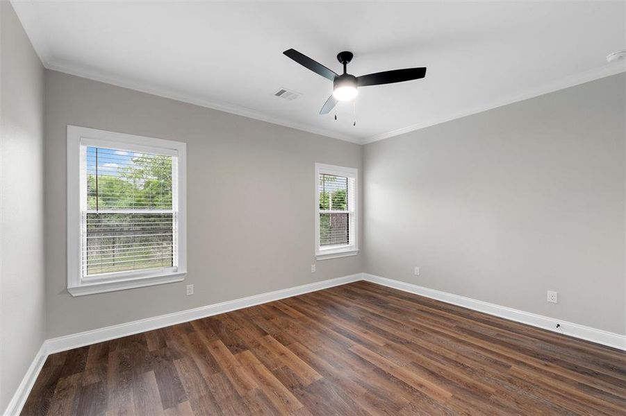 Spare room featuring crown molding, ceiling fan, baseboards, visible vents, and dark wood-style floors
