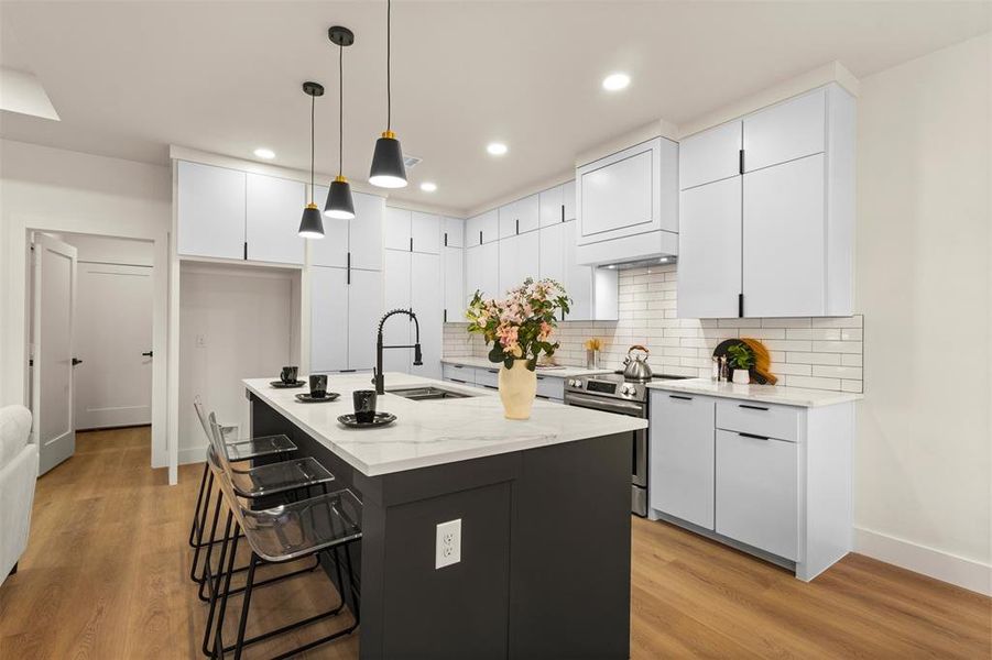 Kitchen featuring white cabinets, hanging light fixtures, decorative backsplash, electric stove, and a breakfast bar area