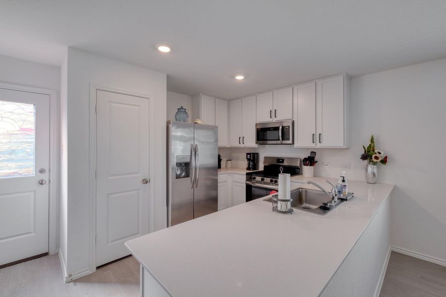 This kitchen features white cabinetry, stainless steel appliances, and a light-colored countertop with an integrated sink