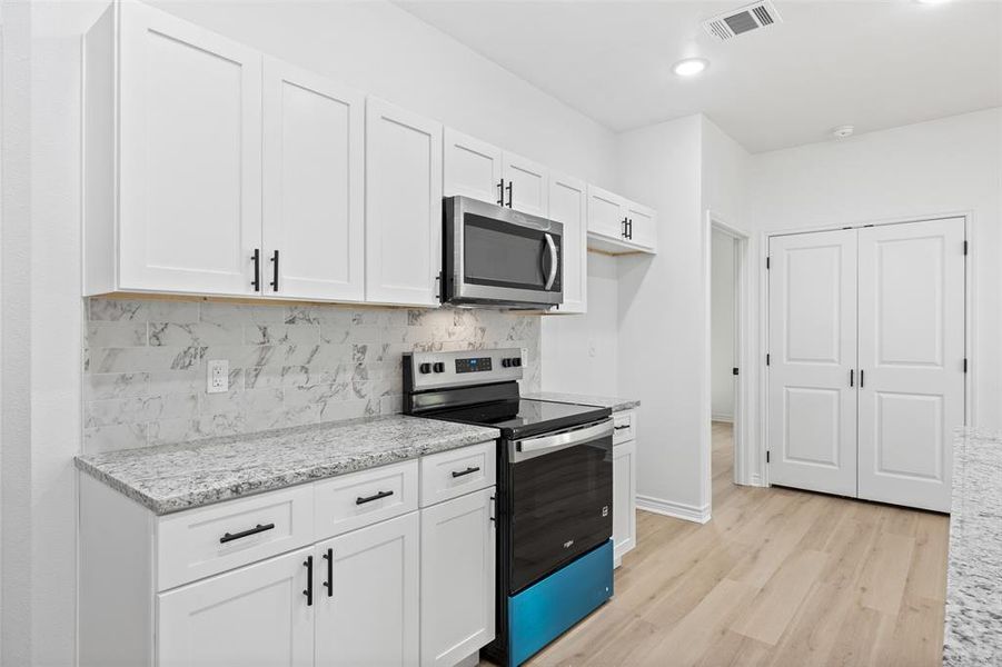 Kitchen featuring stainless steel appliances, decorative backsplash, light wood finished floors, white cabinetry, and light stone countertops