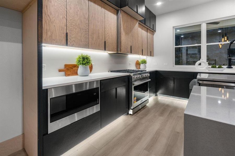 Kitchen with appliances with stainless steel finishes, dark cabinetry, light stone countertops, light wood finished floors, and modern cabinets