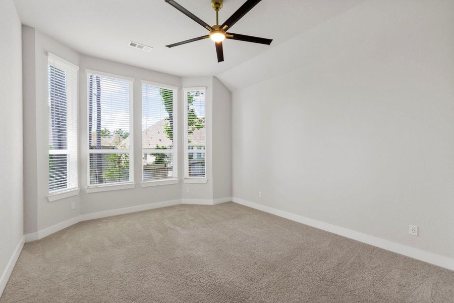 Sunny bedroom with vaulted ceiling, modern fan, and bay-style windows that brighten every morning.