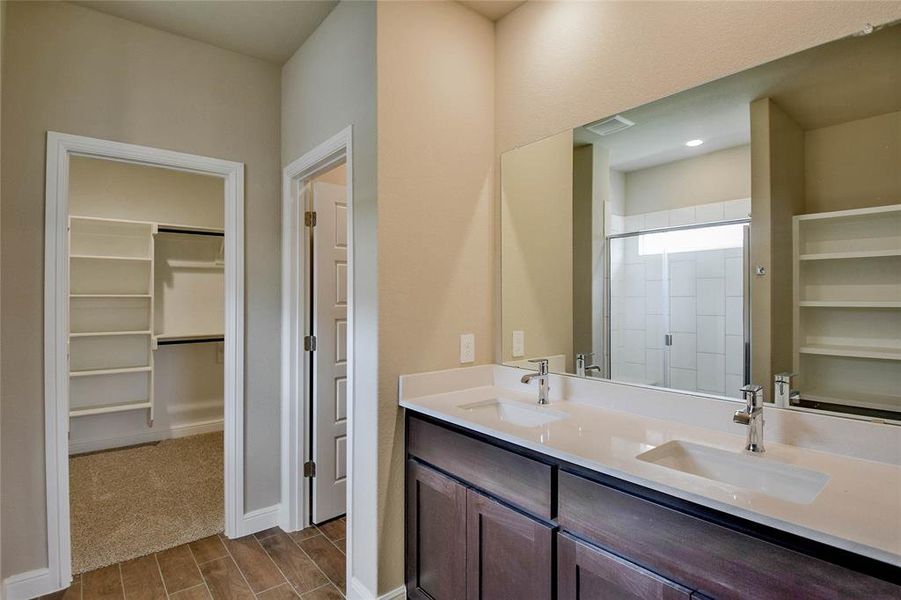 Full bathroom featuring wood finish floors, double vanity, a walk in closet, and a shower stall Full bathroom featuring wood finish floors, double vanity, a walk in closet, and a shower stall