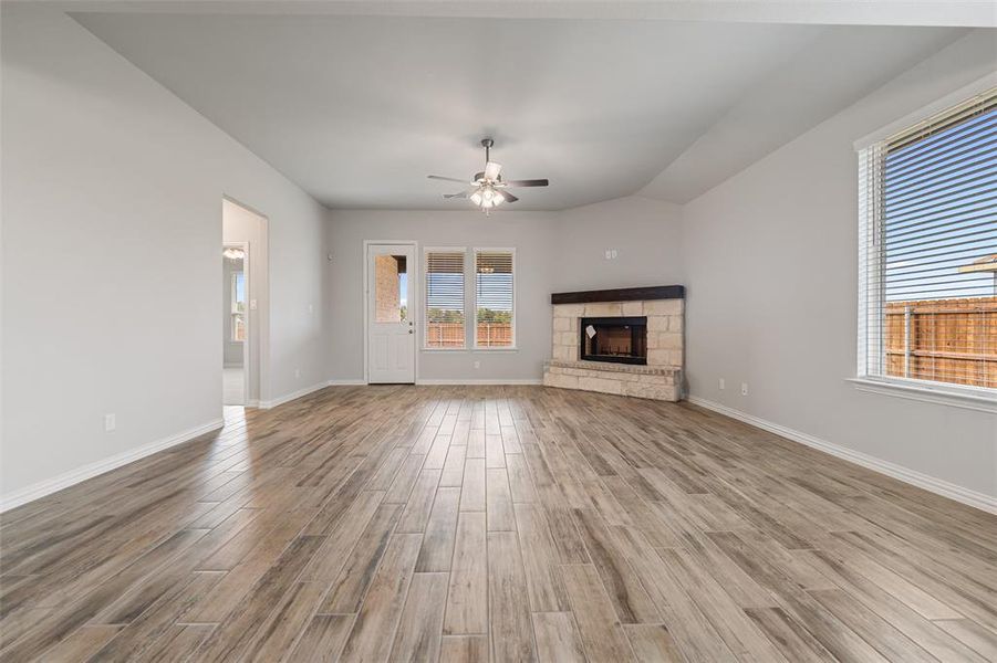 Unfurnished living room with a stone fireplace, wood finished floors, and a ceiling fan Unfurnished living room with a stone fireplace, wood finished floors, and a ceiling fan