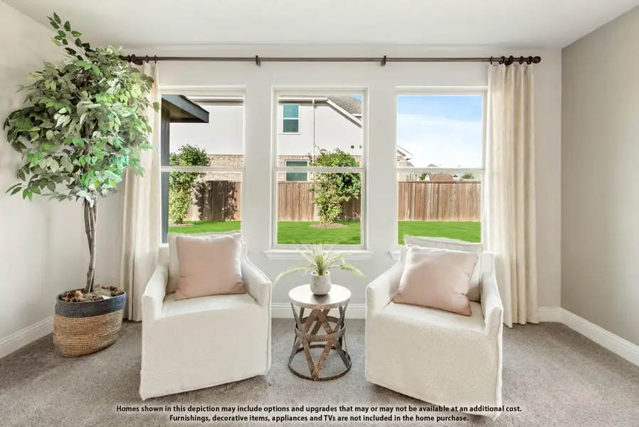 Sitting area with two white armchairs, small side table, and large windows overlooking a fenced backyard