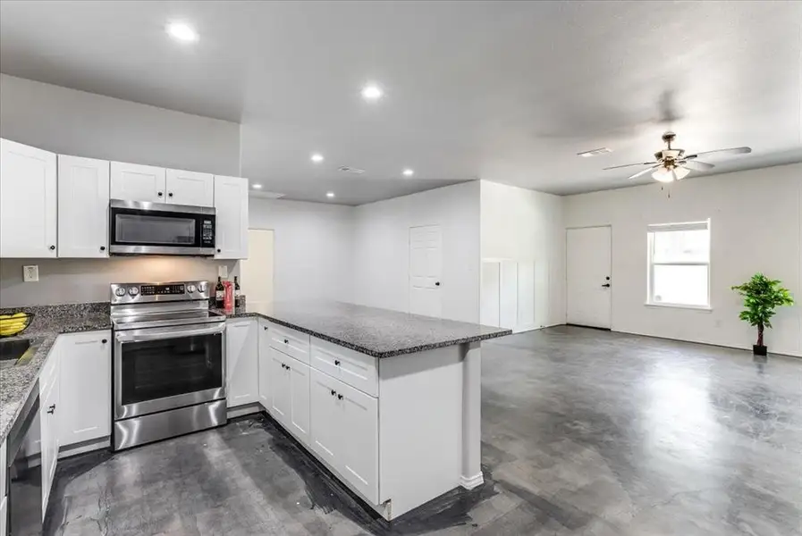 Open-concept kitchen and living area featuring white cabinetry, dark speckled countertops, and stainless steel appliances