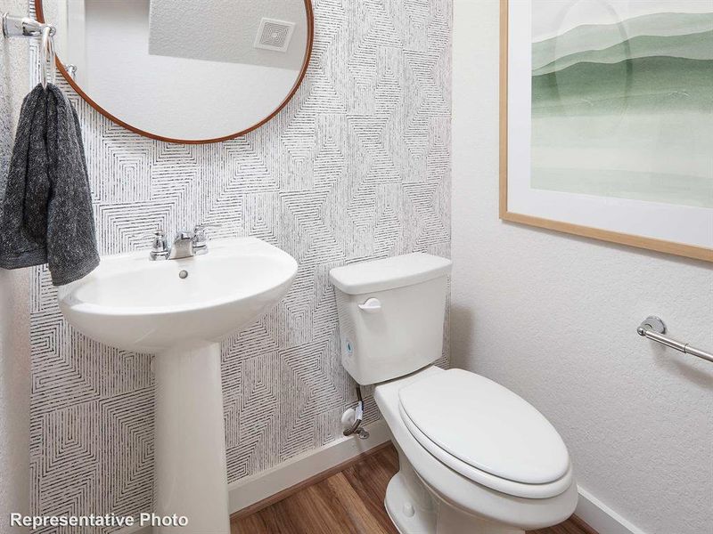 Bathroom featuring a white pedestal sink with a chrome faucet, a round mirror with a wood frame, and patterned wallpaper