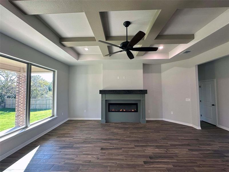 Unfurnished living room with coffered ceiling, dark wood-type flooring, a lit fireplace, beamed ceiling, and ceiling fan Unfurnished living room with coffered ceiling, dark wood-type flooring, a lit fireplace, beamed ceiling, and ceiling fan