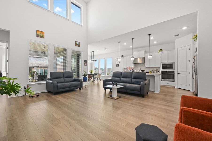 Sunlight streams through upper-level windows into an airy living area with light-toned wood flooring.