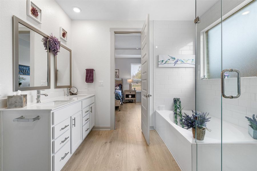 Bathroom featuring healthy amount of natural light, light wood-type flooring, double vanity, and a bath Bathroom featuring healthy amount of natural light, light wood-type flooring, double vanity, and a bath