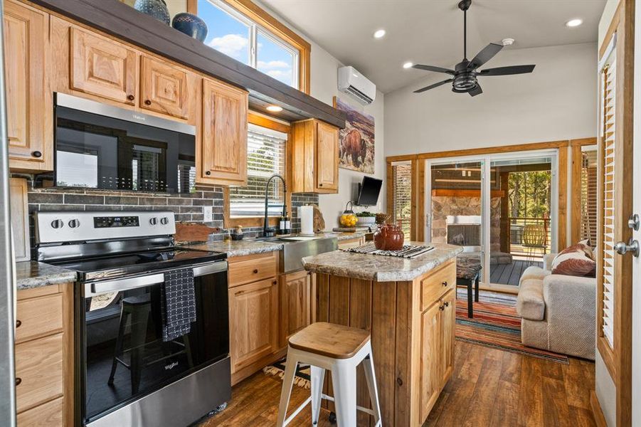 Kitchen featuring stainless steel electric range oven, black microwave, backsplash, dark wood finished floors, and a center island