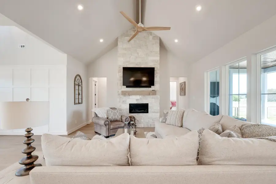 Living area with ceiling fan, wood finished floors, and a stone fireplace