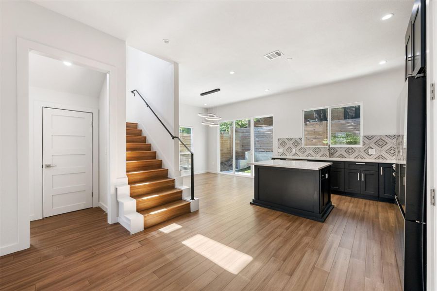 Kitchen with dark cabinets, backsplash, light stone countertops, a kitchen island, and light wood-type flooring