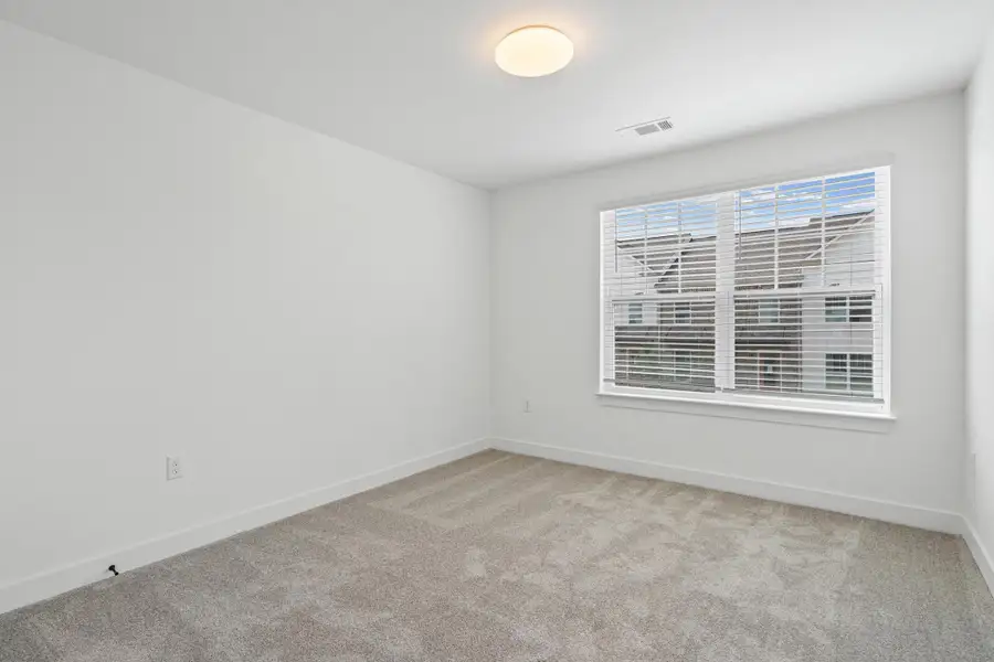 Room featuring light gray carpeting, crisp white walls, a large window with white blinds, and a flush-mount ceiling light