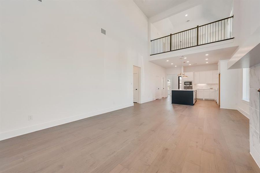 Unfurnished living room featuring light wood-style floors, a high ceiling, and recessed lighting Unfurnished living room featuring light wood-style floors, a high ceiling, and recessed lighting