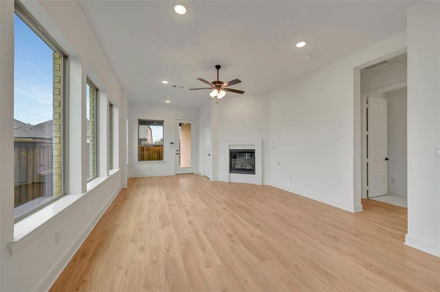 Spacious room featuring wood-finish flooring, multiple large windows, a ceiling fan, recessed lighting, and a built-in fireplace