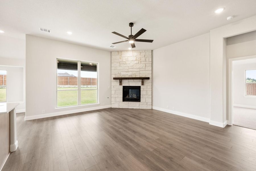 Open living room with wood floors, stone corner fireplace, dark wood mantel, and ceiling fan