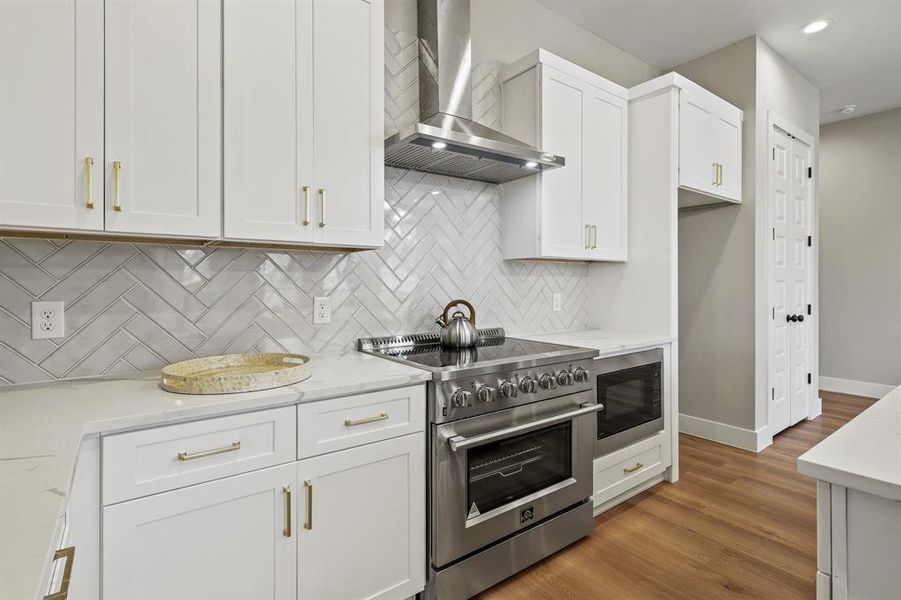 Kitchen with wall chimney exhaust hood, built in microwave, white cabinets, and high end stainless steel range