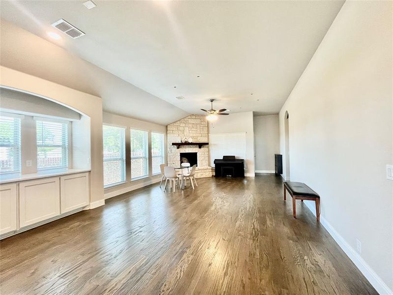 Living room featuring ceiling fan, vaulted ceiling, hardwood / wood-style floors, and a stone fireplace