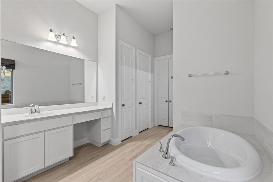 Full bath with a bath, vanity, light wood finished floors, and a closet Full bath with a bath, vanity, light wood finished floors, and a closet