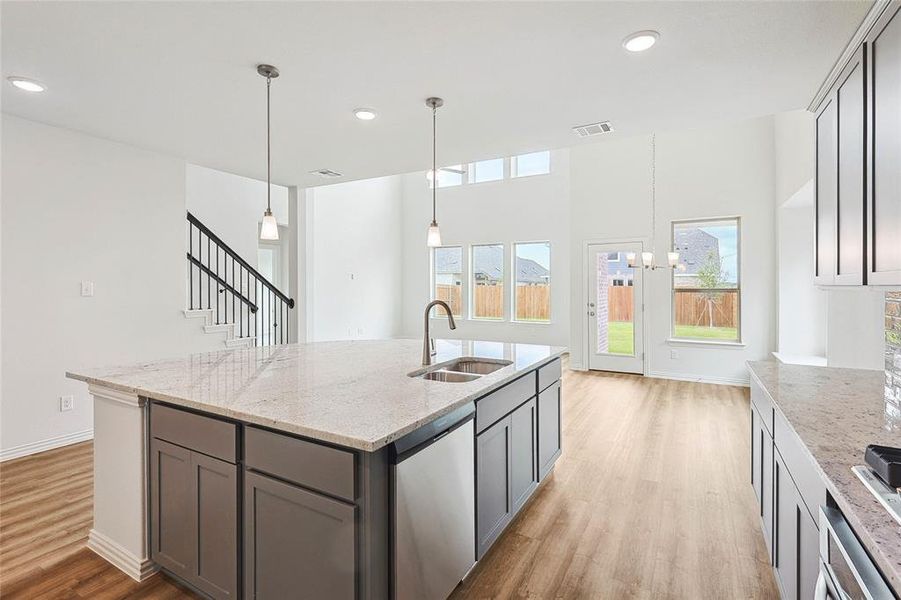 Kitchen featuring hanging light fixtures, light wood-type flooring, light stone counters, sink, and dishwasher