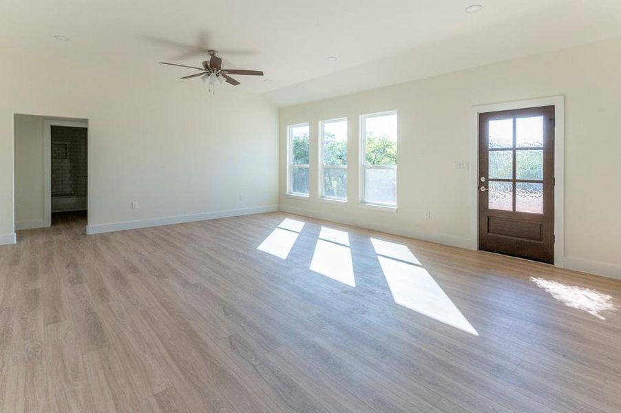 Unfurnished living room featuring healthy amount of natural light, light wood finished floors, lofted ceiling, ceiling fan, and recessed lighting