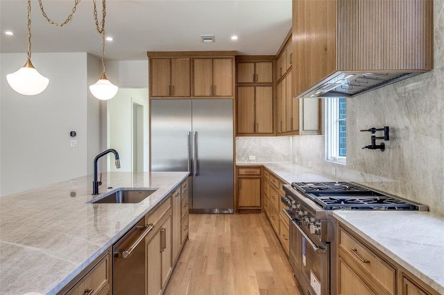 Kitchen with light stone countertops, high quality appliances, decorative light fixtures, light wood finished floors, and recessed lighting Kitchen with light stone countertops, high quality appliances, decorative light fixtures, light wood finished floors, and recessed lighting