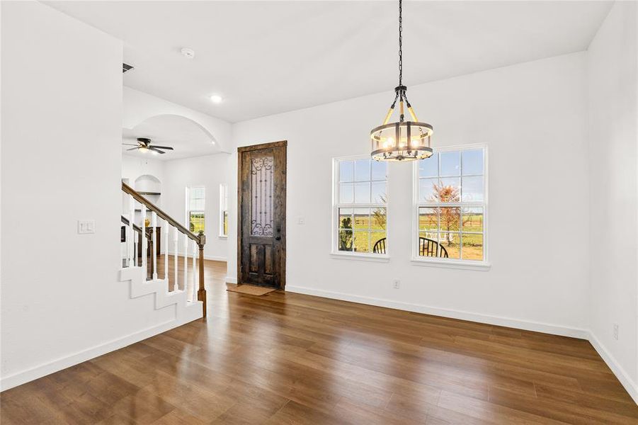 Open-concept interior featuring wood-finish flooring, a decorative entry door, and a staircase with white risers and a dark wood handrail